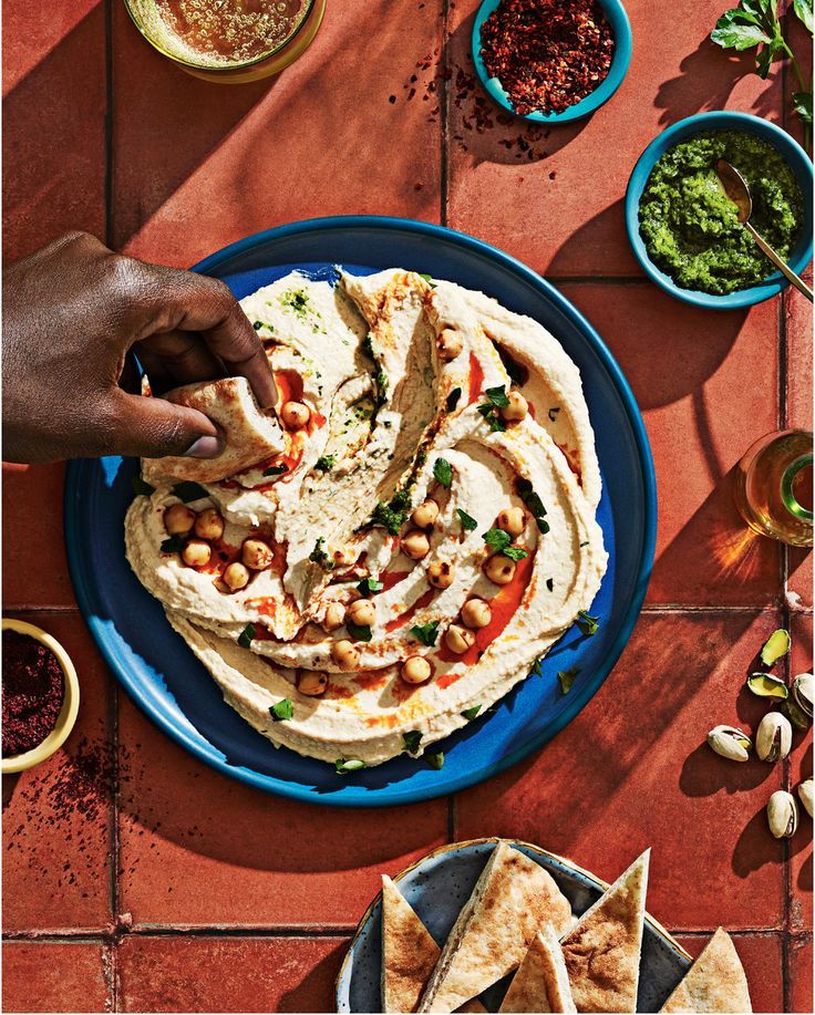 Hand dipping bread into hummus on a terracotta table